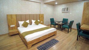 Habitación de hotel con una cama de madera, un escritorio con sillas, un equipo de aire acondicionado y un enchufe.