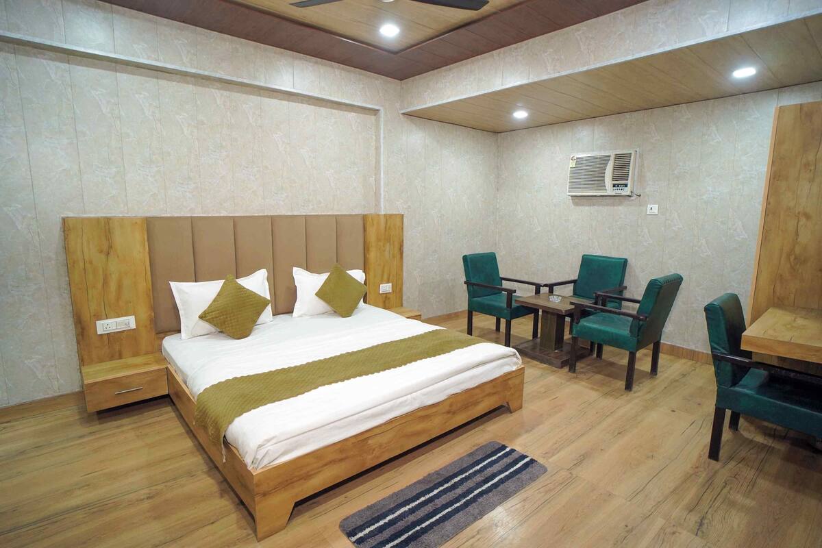 A hotel room with a wooden bed, a desk with chairs, an air conditioning unit, and a power outlet.