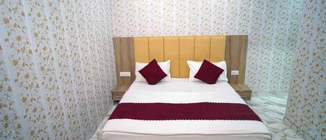 Una cama con cabecera de madera, dos almohadas y una manta roja.