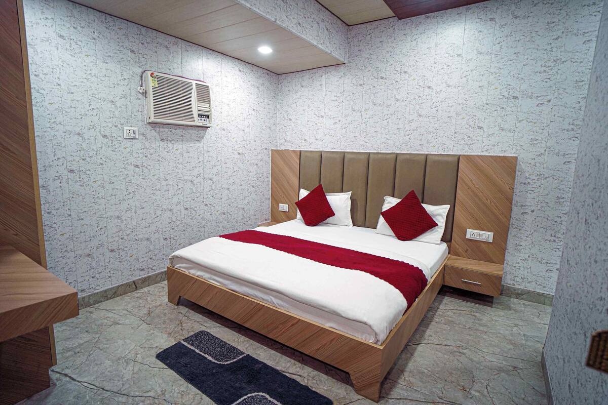A bedroom with a bed, a nightstand, a wall-mounted air conditioner, and a patterned wall.