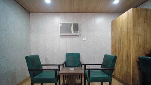 Habitación con techo de madera, aire acondicionado de pared, un armario de madera y una mesa con dos sillas verdes.
