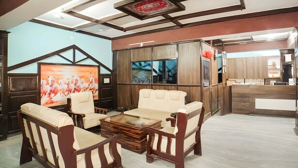 Un hall de hotel con mostrador de recepción, zona de estar con sofás y sillones, un cuadro grande y una estructura de techo de madera.