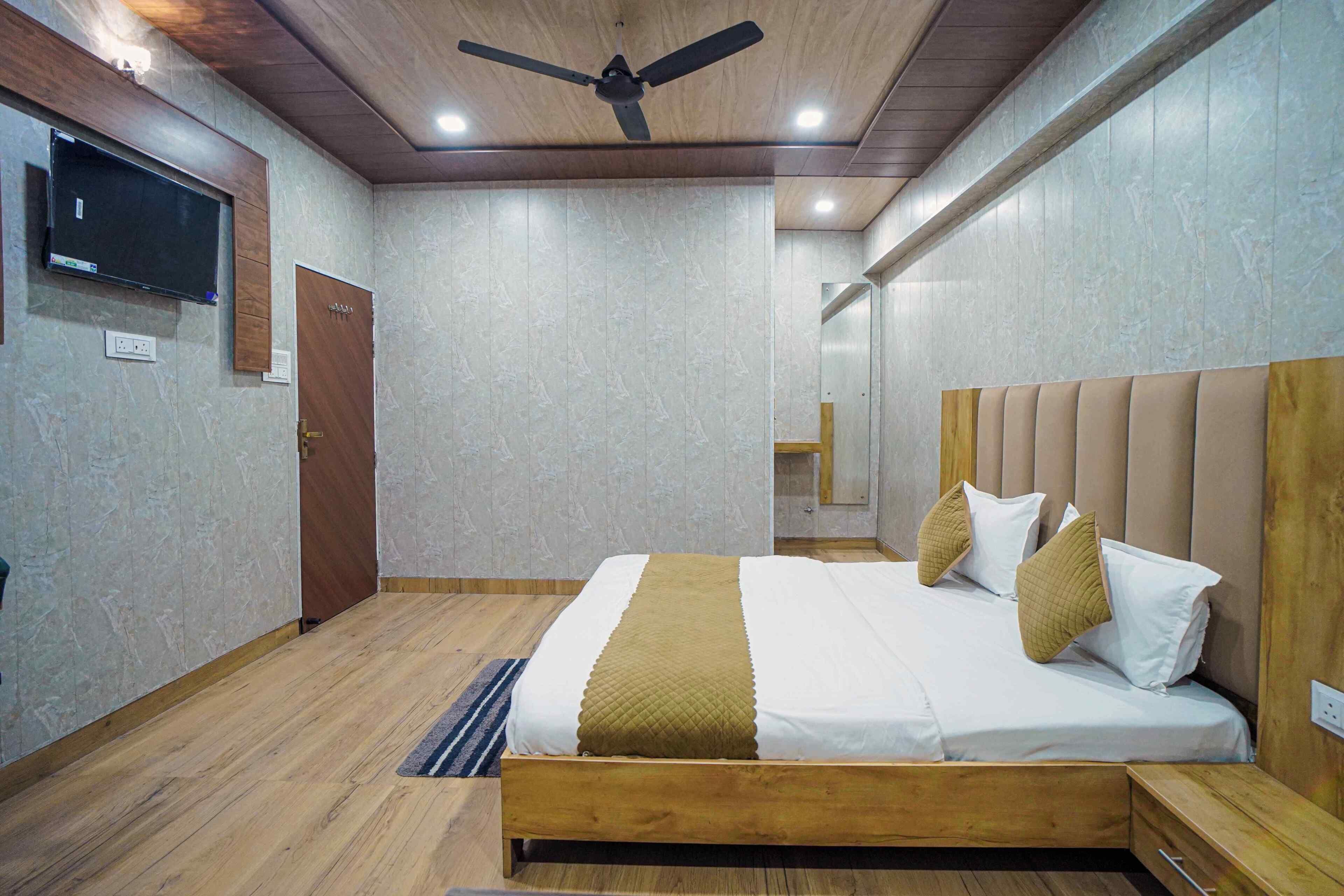 Una camera da letto con un letto di legno, una ventola a soffitto, una TV a parete e una porta.