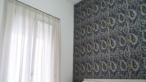 Een slaapkamer met een bed, nachtkastje, lamp en raam met dunne gordijnen.