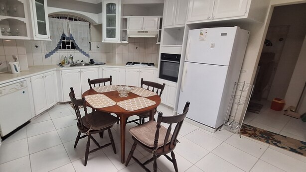 A compact kitchen with white cabinetry, a dining table with four chairs, a microwave, a toaster, and a refrigerator. - Cottage at Coverley (Christ Church)