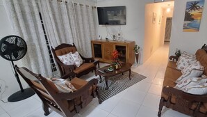A living room with a sofa, two armchairs, a coffee table, a TV, and a fan. - Cottage at Coverley (Christ Church)