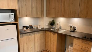 A kitchen with wooden cabinets, a microwave, a refrigerator, a sink, and a kettle. - Zenao Appart'hôtels Cognac (Cognac)