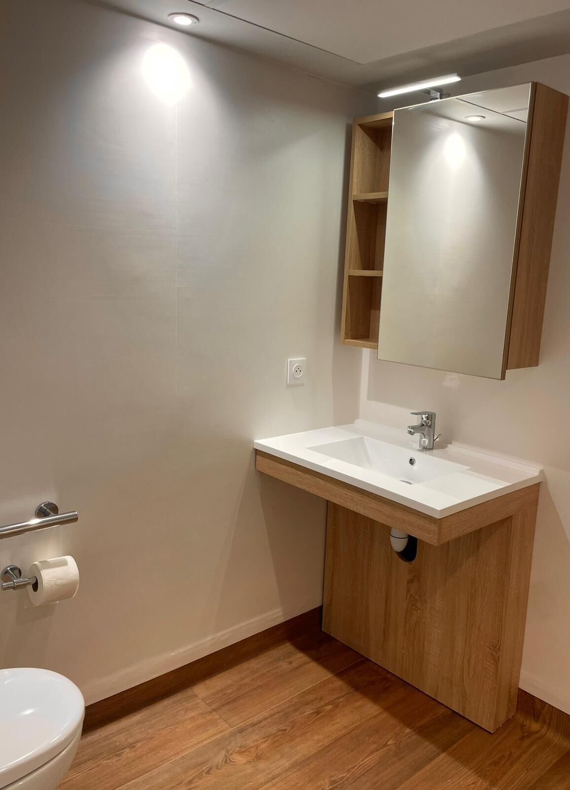 Een badkamer met een witte wastafel, houten opbergmeubel en een spiegel.