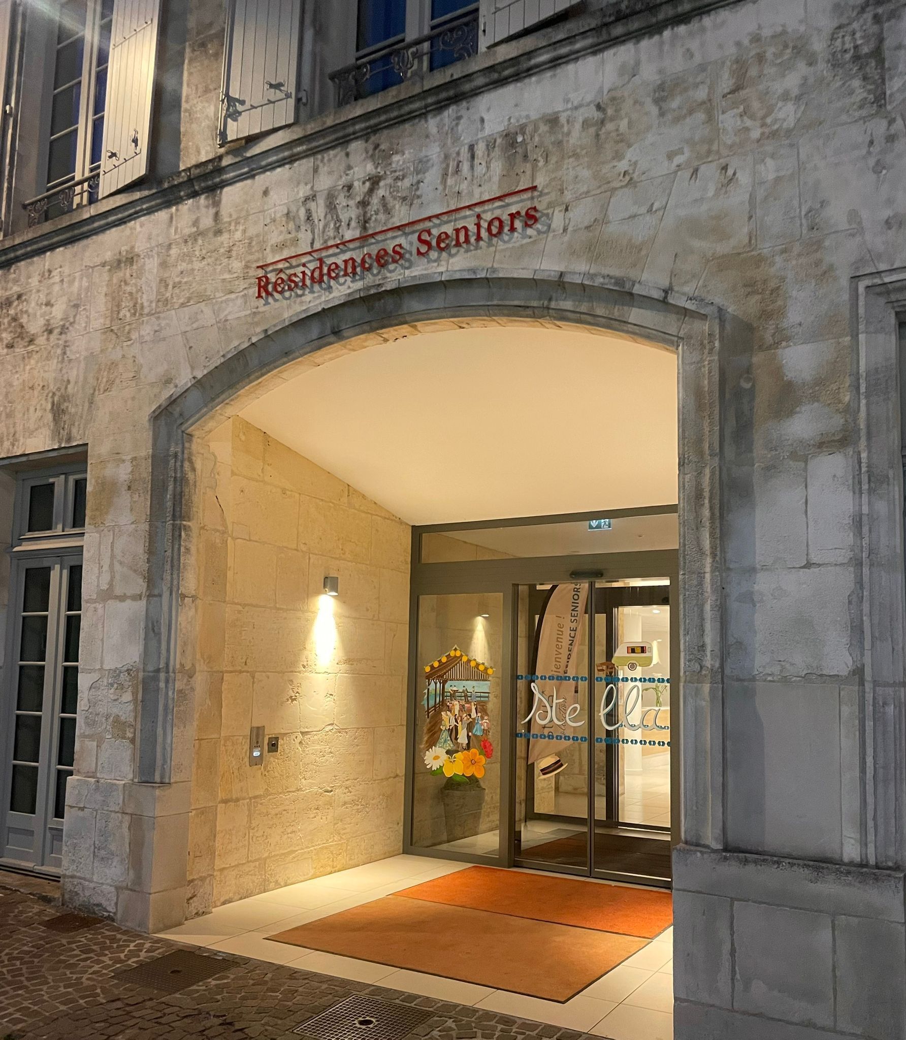A hotel entrance with a stone facade, an archway, and a sign reading "Residences Seniors".