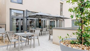 An outdoor patio area with tables and chairs, umbrellas, and a potted plant. - Zenao Appart'hôtels Cognac (Cognac)