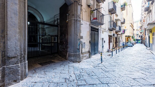A cobblestone street with historic buildings, a gated entrance, and balconies with plants. - Modern Spacious Apartment in the Heart of Naples (Naples)