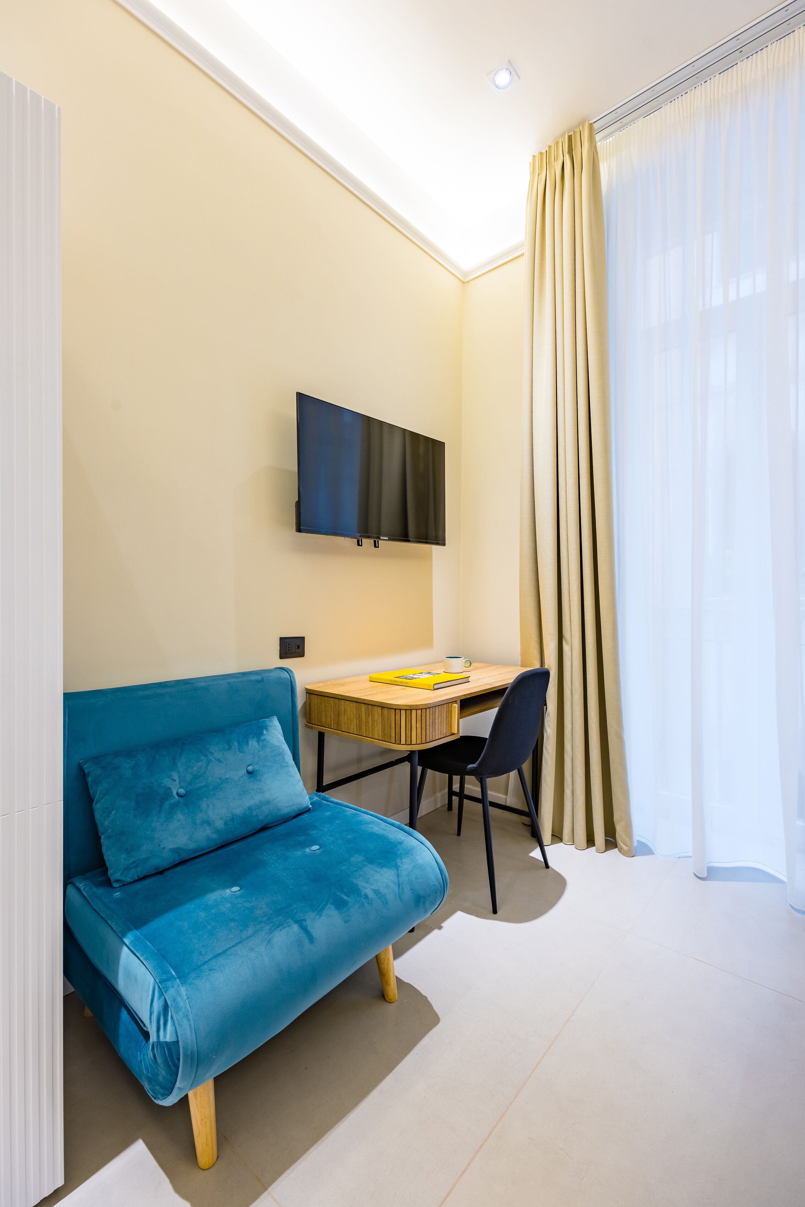 Ein modernes Zimmer mit einem blauen Sofa, einem Holztisch, einem Flachbildfernseher und einem großen Fenster mit Vorhängen.