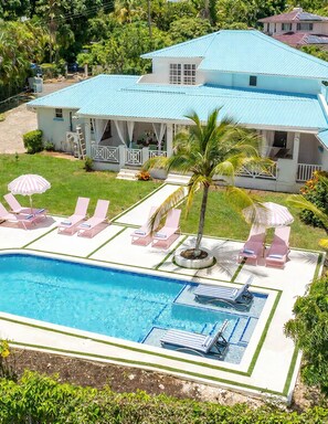 A pool area with lounge chairs and umbrellas, surrounded by a well-maintained lawn and a house with a blue roof.