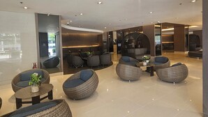 Un vestíbulo moderno con sofás de mimbre redondos, una zona de estar central y un separador de vidrio.