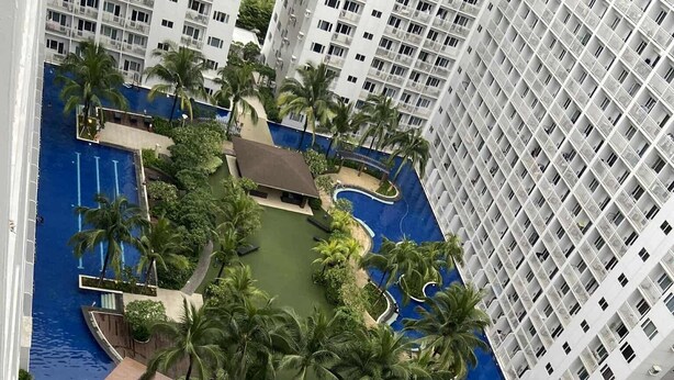 Un hotel de gran altura con piscina central rodeada de palmeras y una zona de juegos para niños.