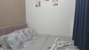 Una habitación de hotel con cama, cabecero, una pared con tres obras de arte enmarcadas y una ventana con cortinas.