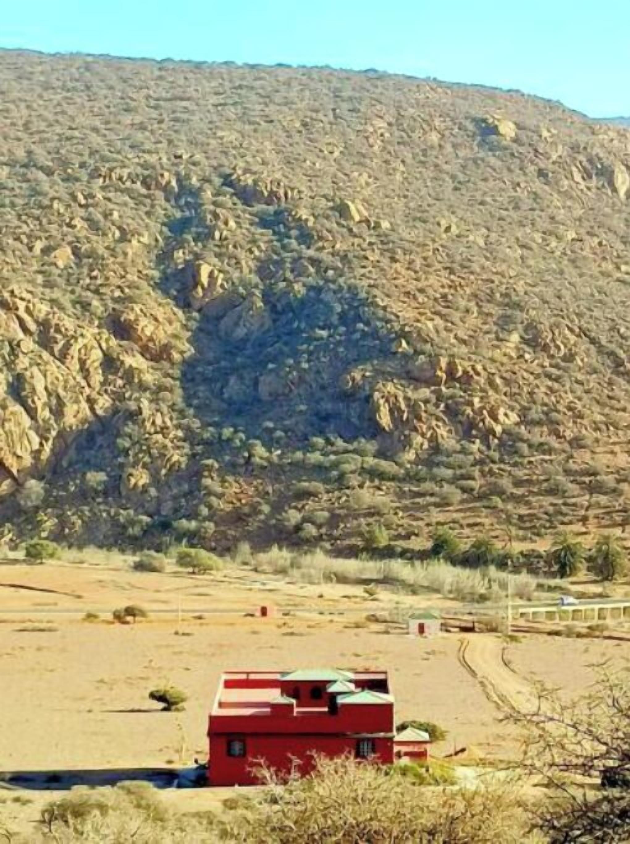 A red building with a flat roof, surrounded by a dry, rocky landscape with sparse vegetation.