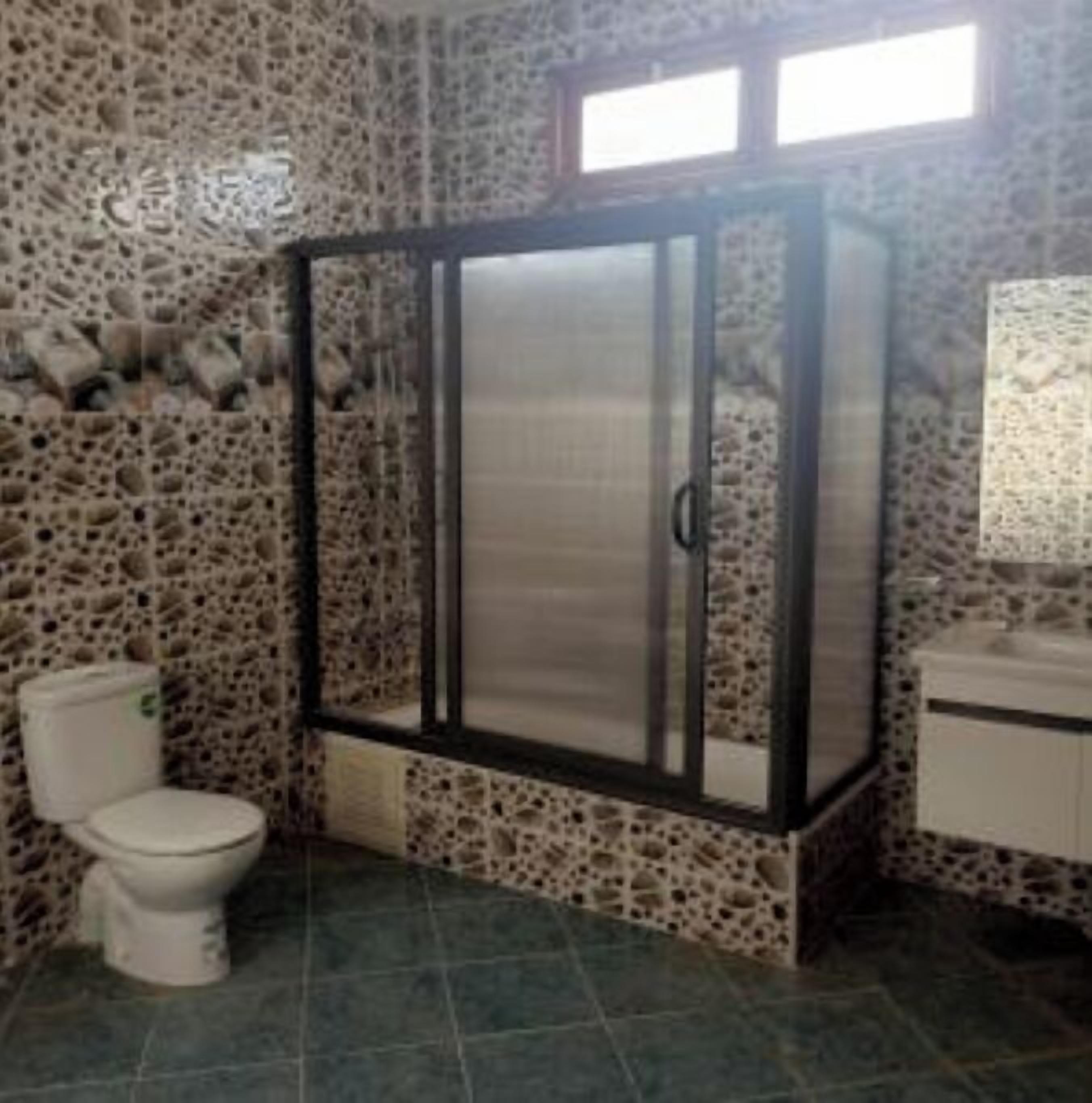 Une salle de bain avec un mur en pierre, des toilettes, un meuble et une fenêtre.