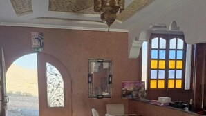 A dining area with a checkered floor, a table with chairs, a decorative mirror, and a window with yellow panes. - Auberge Assif iboudrarn (Tioughza)