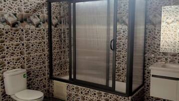 Un baño con pared de piedra, inodoro, cabina de ducha y lavamanos.
