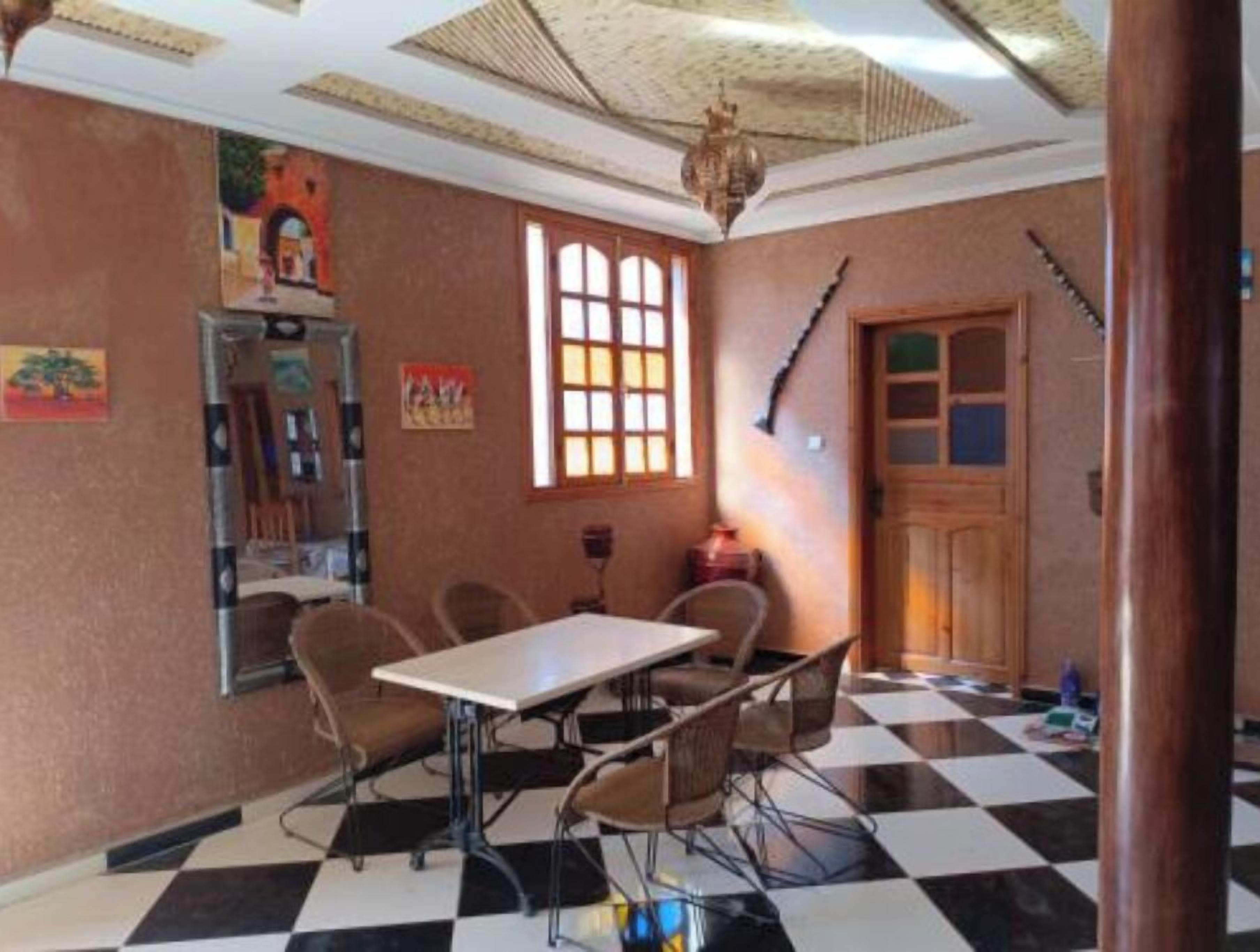 Una habitación con piso a cuadros, una mesa con sillas, una puerta de madera y una ventana con vista.