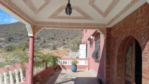 A covered outdoor area with a patterned ceiling, a lantern, a potted plant, and a view of a hilly landscape. - Auberge Assif iboudrarn (Tioughza)
