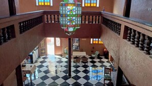 A multi-level interior with a checkered floor, a hanging stained glass light fixture, and a balcony railing. - Auberge Assif iboudrarn (Tioughza)