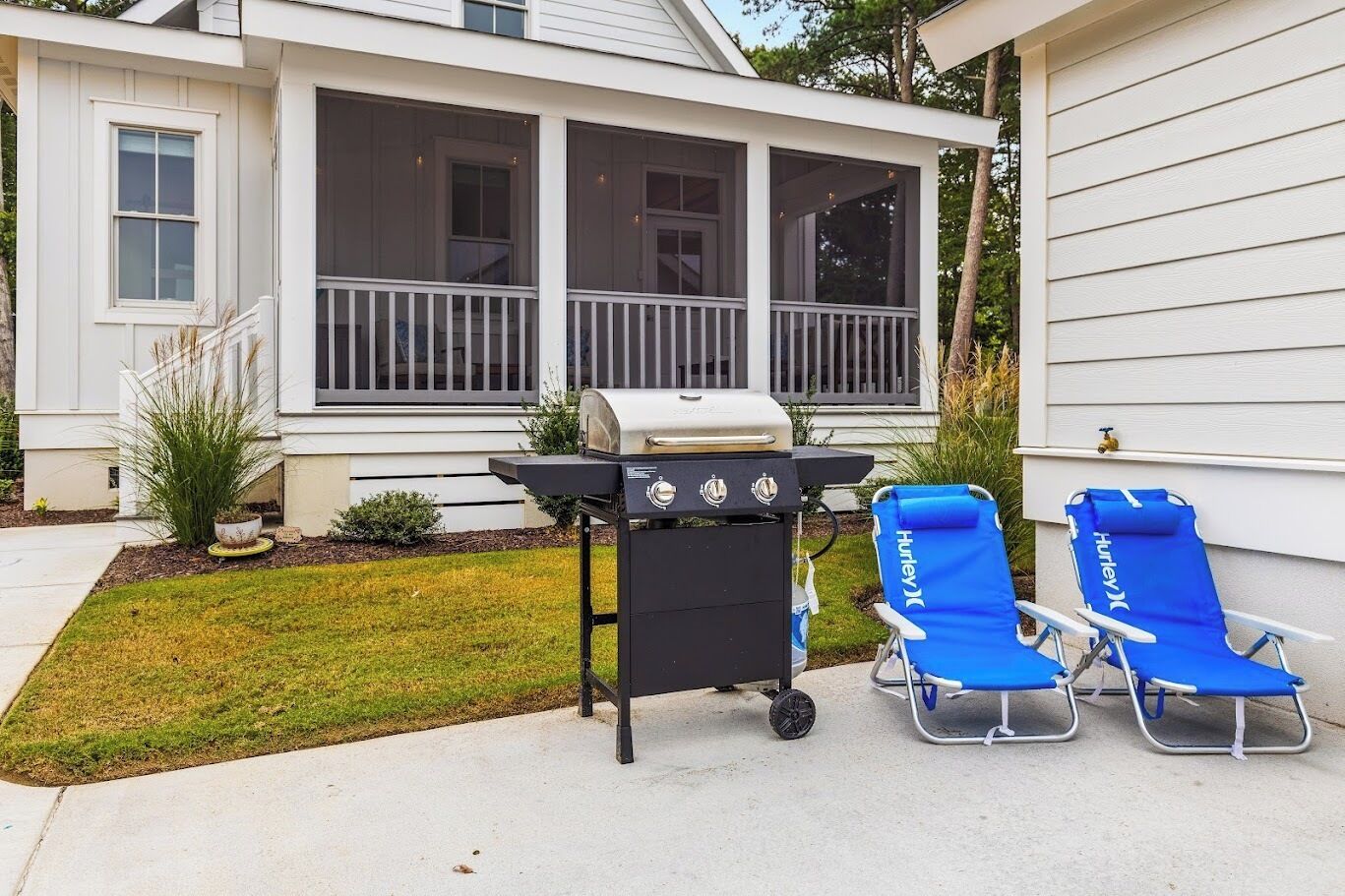 A house with a covered porch, a grill, and two blue lounge chairs.