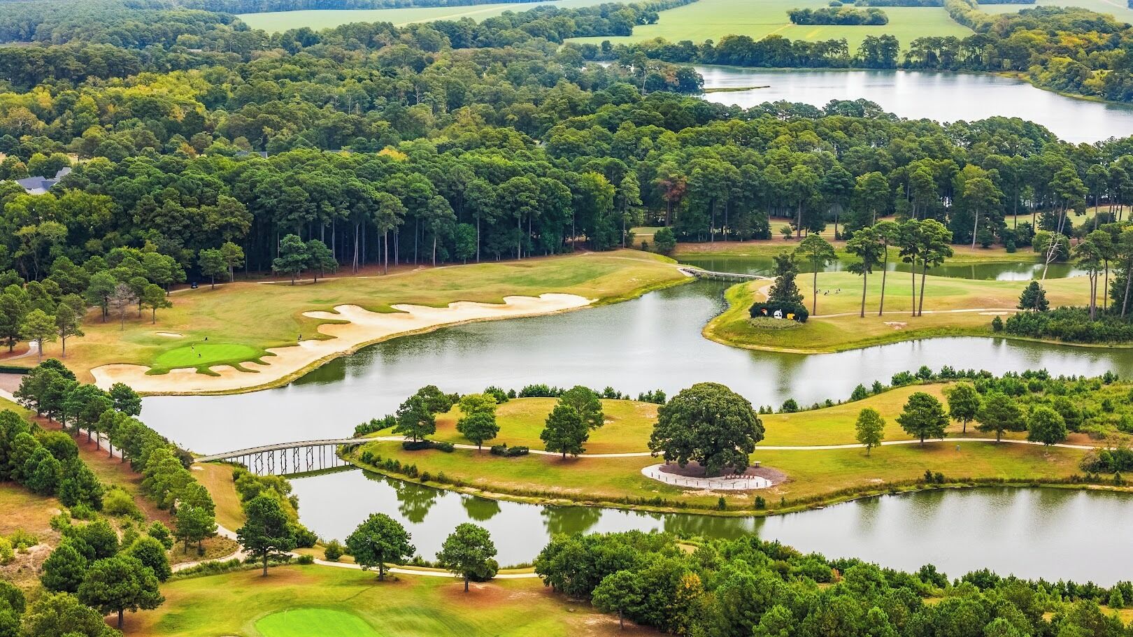 An aerial view of a golf course with multiple ponds, sand bunkers, and a bridge.