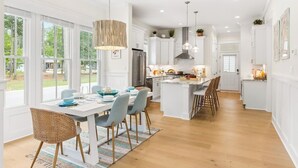 Una cocina moderna con armarios blancos, una isla central y un comedor con un amplio ventanal.