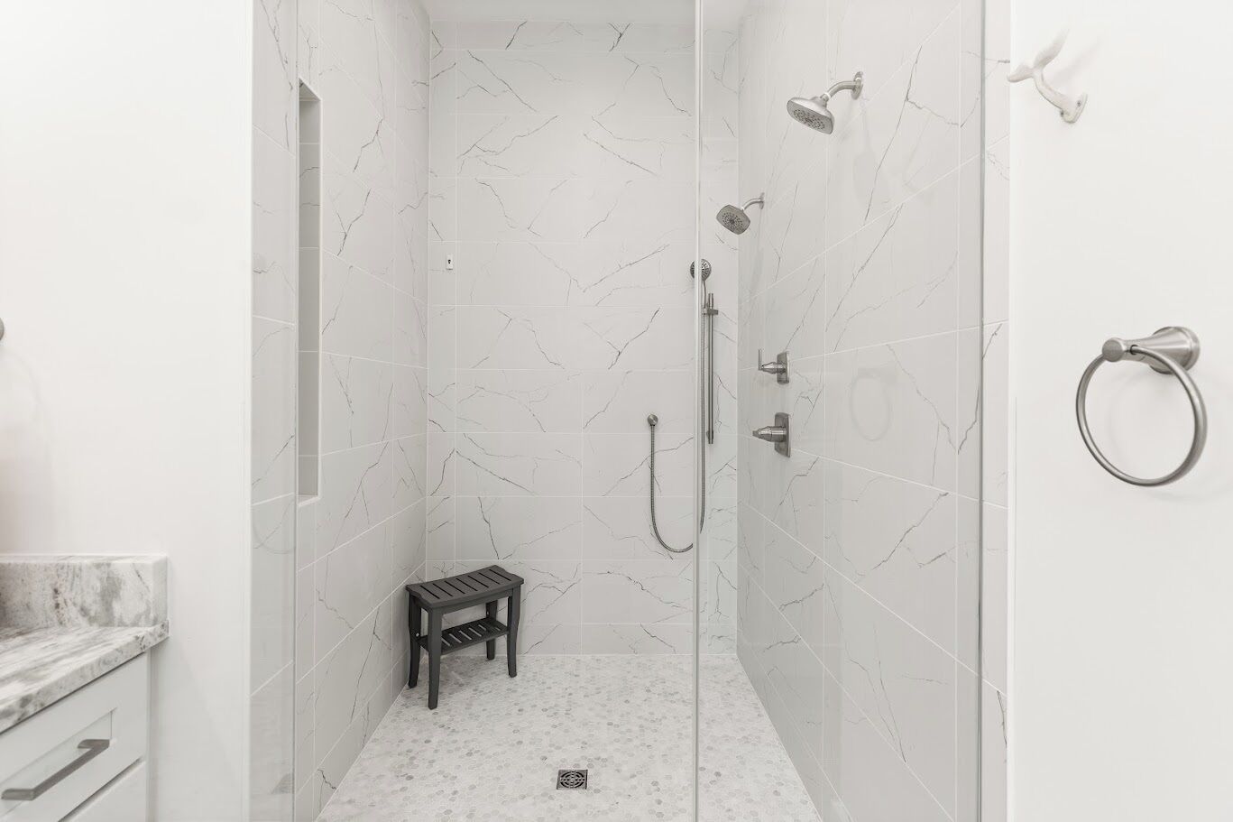 A walk-in shower with white marble tiles, a handheld showerhead, a wall-mounted faucet, and a towel ring.