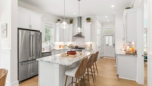 Una cocina moderna con armarios blancos, electrodomésticos de acero inoxidable y una isla central con taburetes de bar.