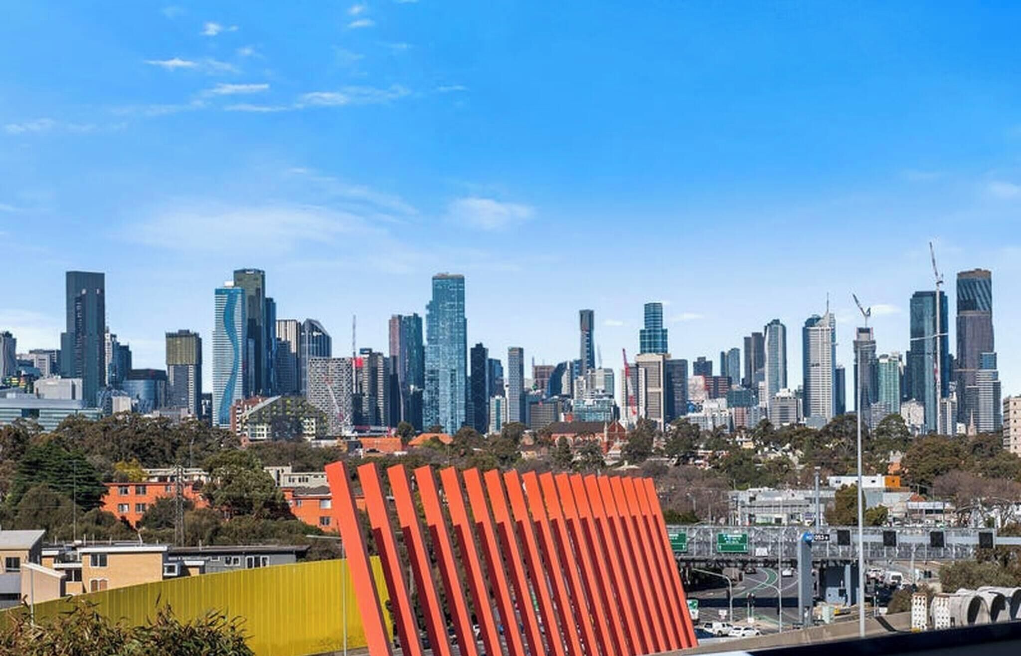 Une vue sur les toits d’une ville, avec des immeubles modernes et des gratte-ciel, et une imposante structure rouge au premier plan.