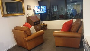 A living room with two brown leather sofas, a wooden cabinet, a television, and a large window with a city view. - Amazing City Views on 18th Floor With car Park (Melbourne)