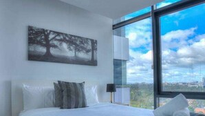 A modern bedroom with a large bed, a city view through the window, and a painting on the wall. - Amazing City Views on 18th Floor With car Park (Melbourne)