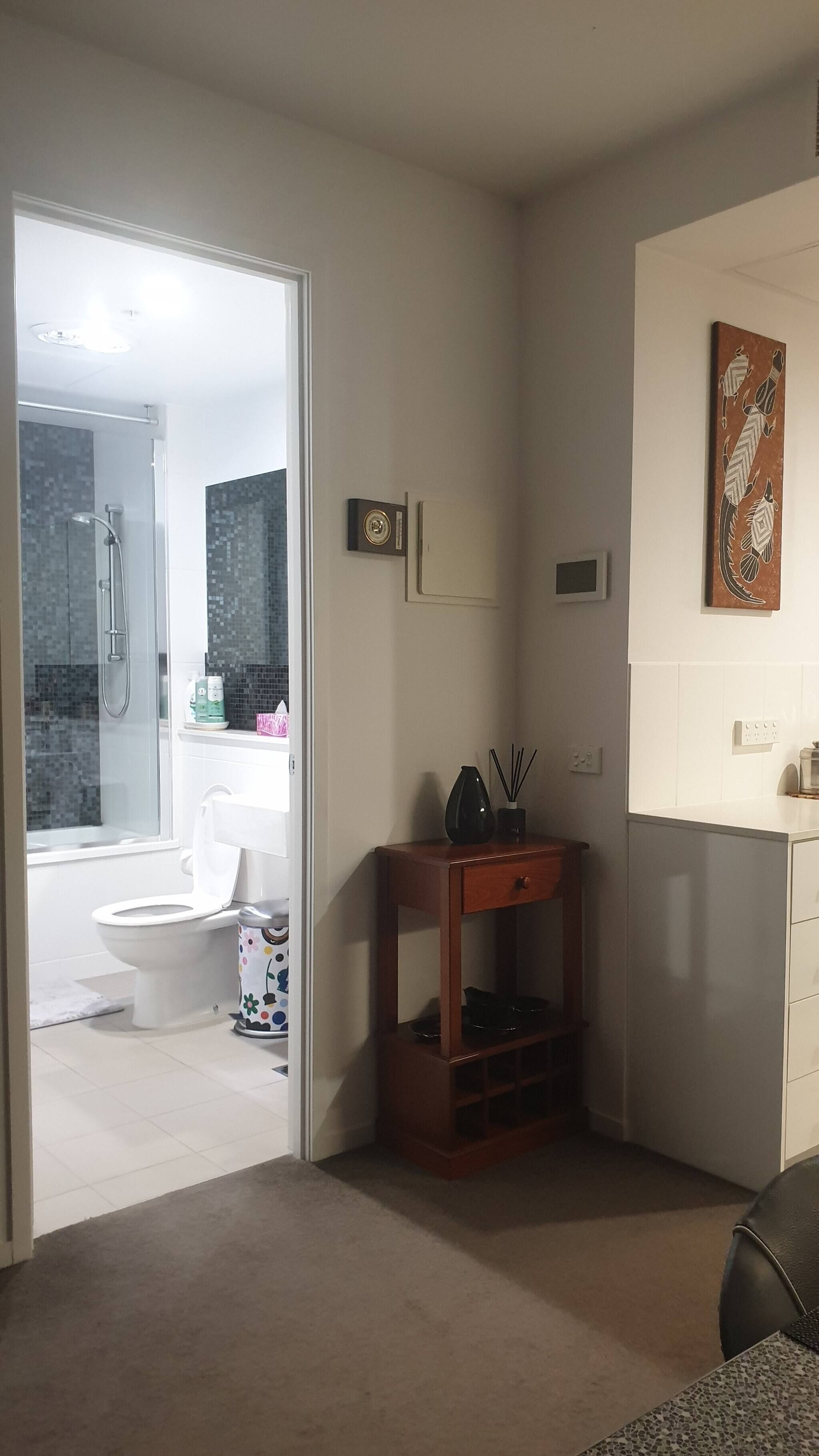 A bathroom with a shower, toilet, and sink. There is a wooden cabinet with a vase and a picture frame on the wall.