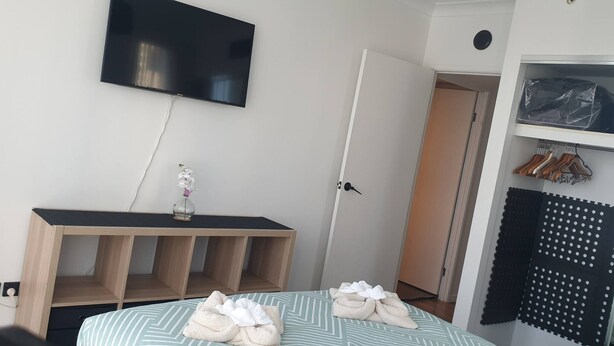 A bedroom with a bed, a TV mounted on the wall, a wooden bedside table, a door, and a closet with hangers. - Chevron With 3beds and own Carpark Within Tower3 (Gold Coast)
