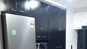 A modern kitchen with a stainless steel refrigerator, black cabinets, and a wooden floor. - Chevron With 3beds and own Carpark Within Tower3 (Gold Coast)