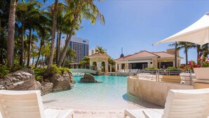 A pool area with lounge chairs, palm trees, and a building with a red roof. - Chevron With 3beds and own Carpark Within Tower3 (Gold Coast)