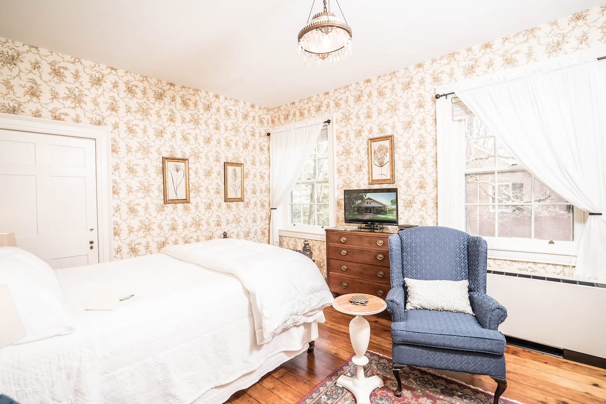 A bedroom with a bed, dresser, chair, and a television.