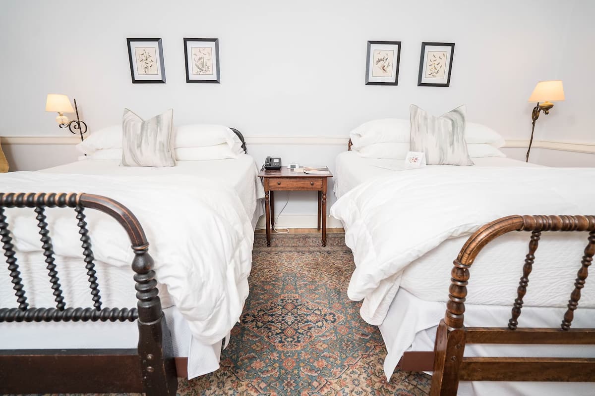 A hotel room with two beds, a nightstand, a lamp, and framed artwork on the wall.