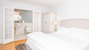 Un dormitorio con una cama grande, un armario, una mesita de noche con lámpara y una maleta en el suelo.