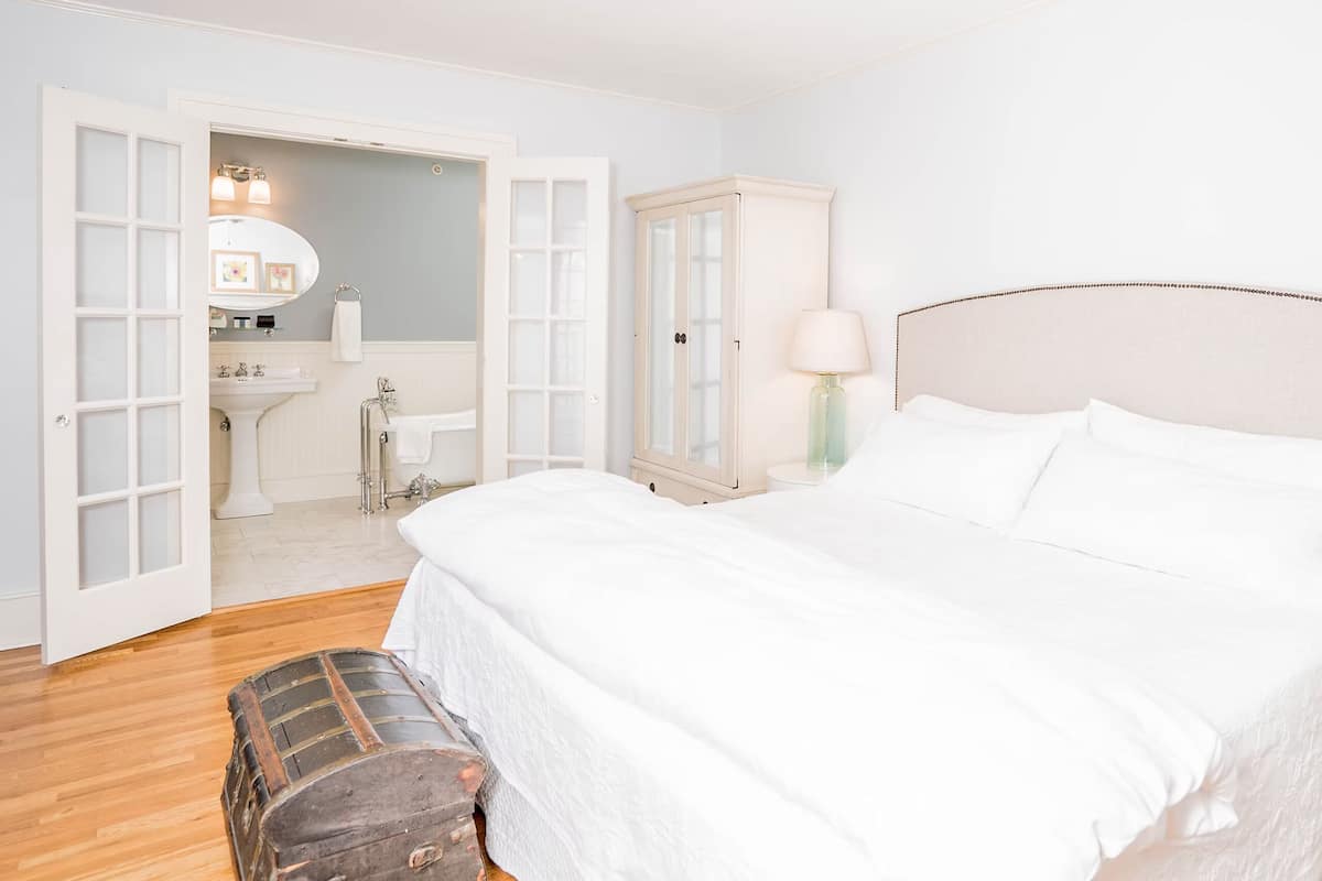 A bedroom with a large bed, a wardrobe, a bedside table with a lamp, and a suitcase on the floor.
