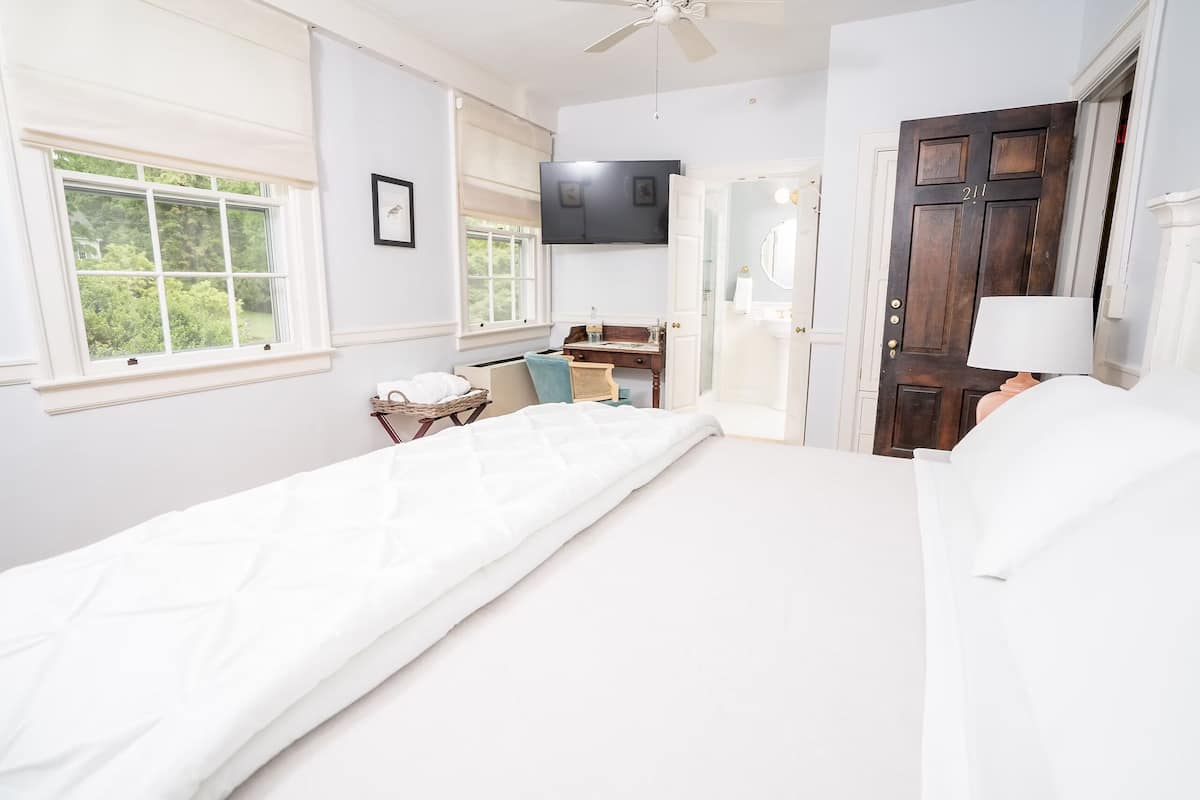 A bedroom with a bed, a desk, a chair, a television, and a door.