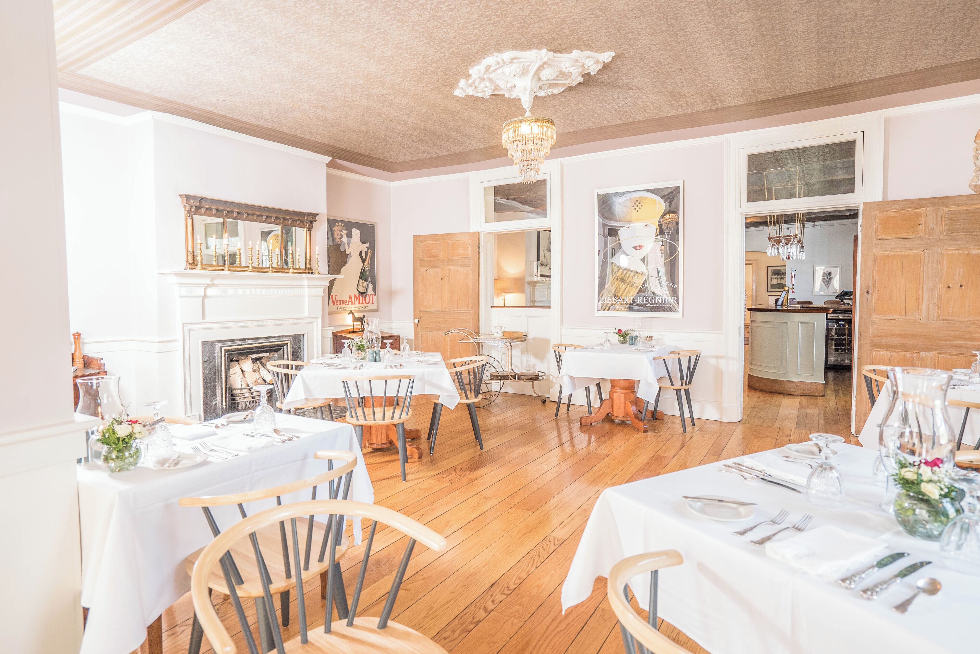 A dining area with multiple tables set for service, wooden flooring, and a chandelier.
