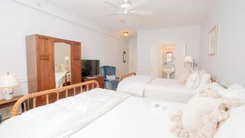 Habitación de hotel con dos camas, un armario de madera, un escritorio con lámpara, un televisor y un ventilador de techo.