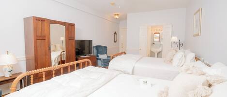 Ein Hotelzimmer mit zwei Betten, einem Holzschrank, einem Schreibtisch mit Lampe, einem Fernseher und einem Deckenventilator.
