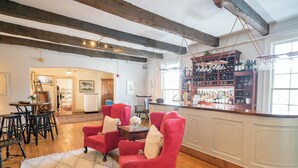 Amplia sala de estar con techo de madera, zona de bar con estantes llenos de botellas y comedor con mesa y sillas.