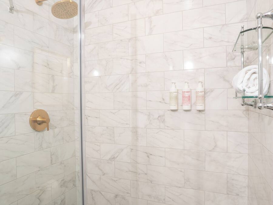 Un baño moderno con ducha acristalada, azulejos de mármol y suelo de baldosas hexagonales.