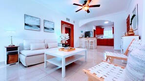 A modern living room with a sofa, coffee table, and a dining area with a kitchen in the background.